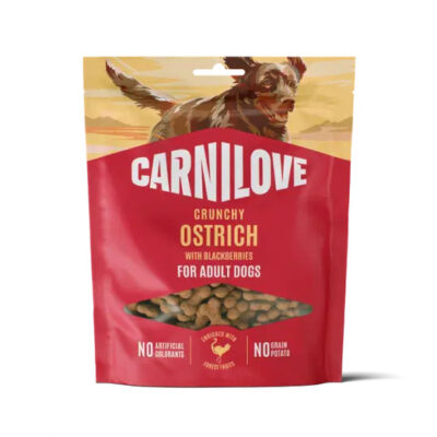 Red Carnilove bag of crunchy ostrich dog treats with blackberries for adult dogs; transparent window shows the treats and a dog image on the top background are yellow-orange skies.